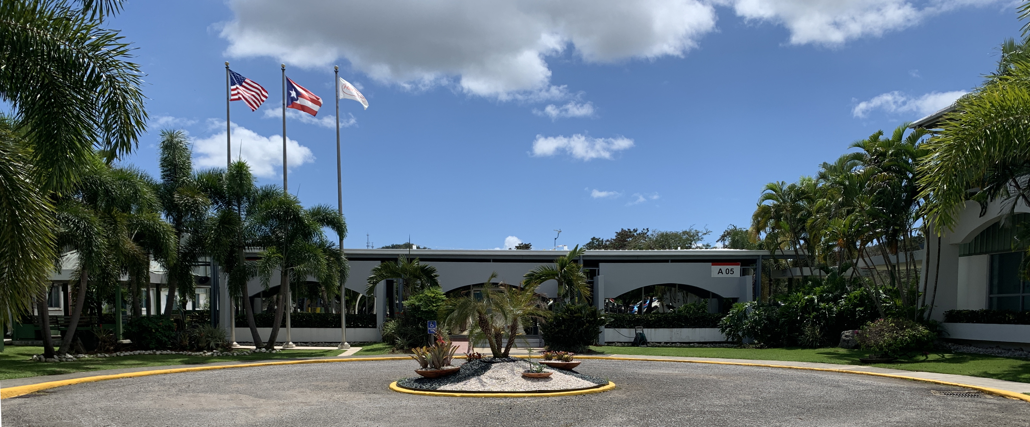 Front exterior view of a manufacturing facility surrounded by lush foliage.