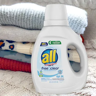 An 'all' brand detergent product is sitting in front of stacked and folded laundry. 