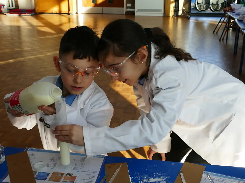 Children in lab coats pouring liquid into a beaker
