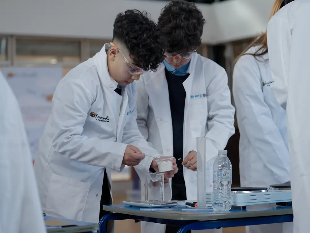 Children in white lab coats measuring materials