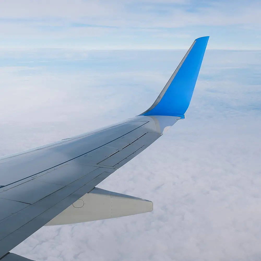 View of an airplane wing with a blue winglet above the clouds.