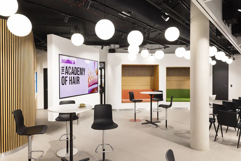 The photo shows a glimpse into the Academy of Hair in Hamburg, featuring several round tables and cozy seating areas.
