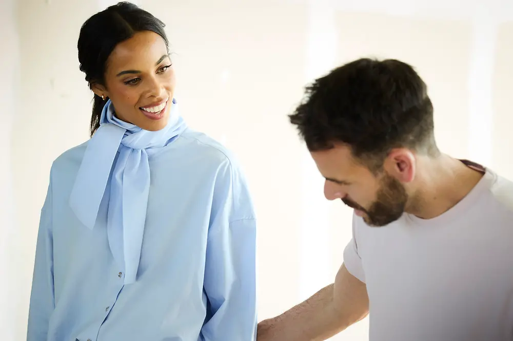 A woman stands next to a man in a fashion show fitting