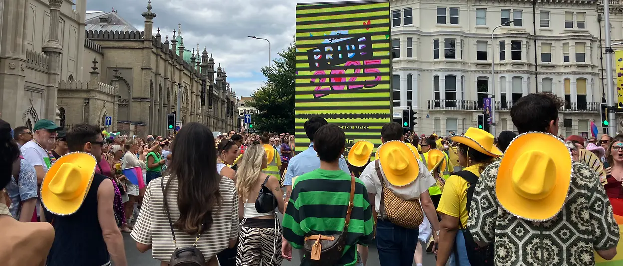 People walking down the street at a parade with a “got2b Pride 2025” screen