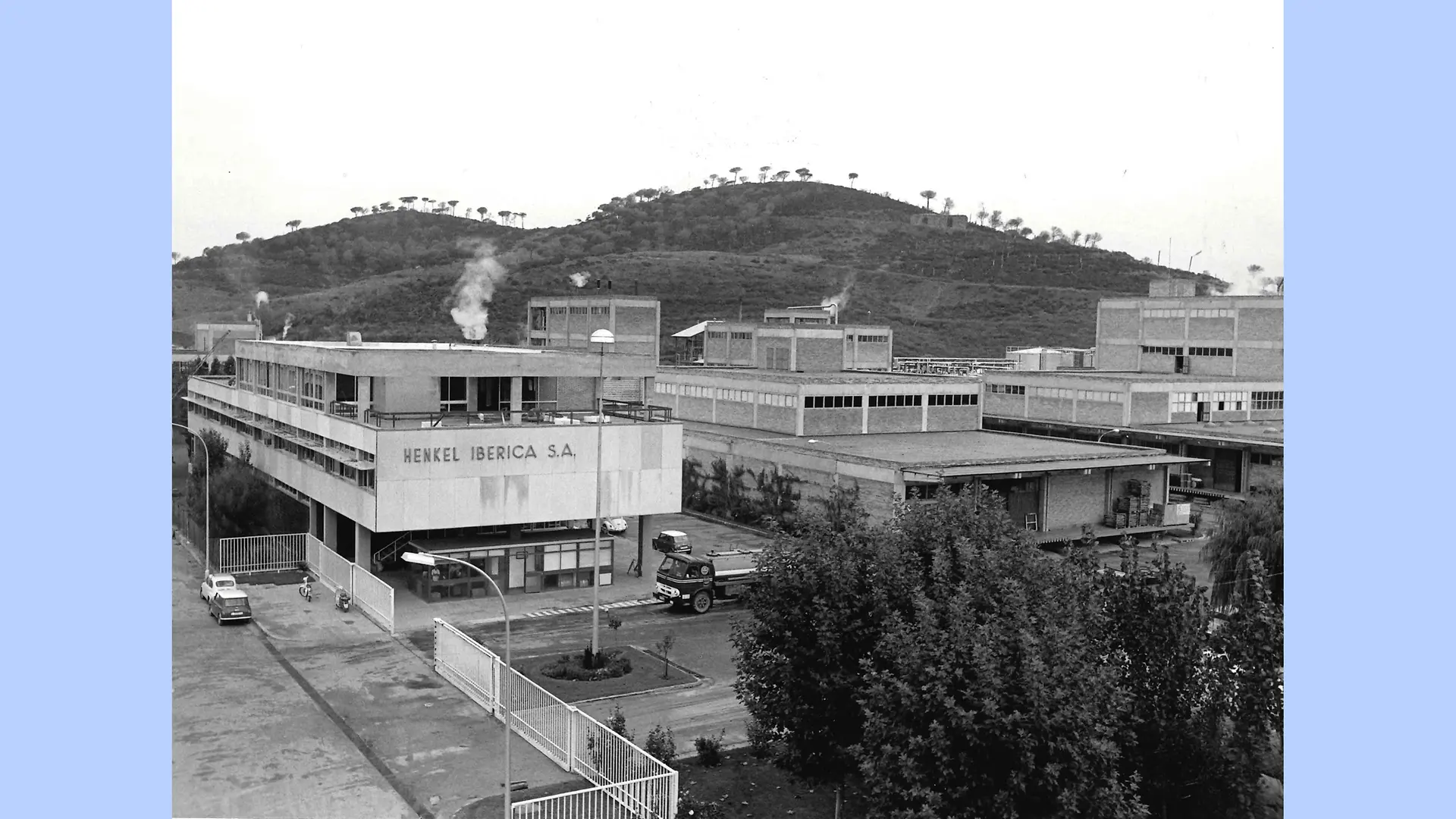 Image en noir et blanc de l’extérieur du site de Montornès. La photo montre le complexe industriel avec ses différents bâtiments entourés par les collines et montagnes de la région