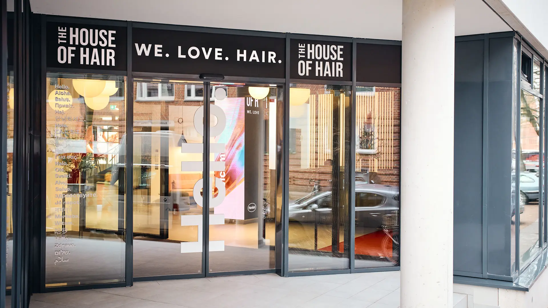 Entrée vitrée. Au-dessus de la porte figure le slogan « We. Love. Hair. ». À droite et à gauche, l’inscription « The House of Hair ».
